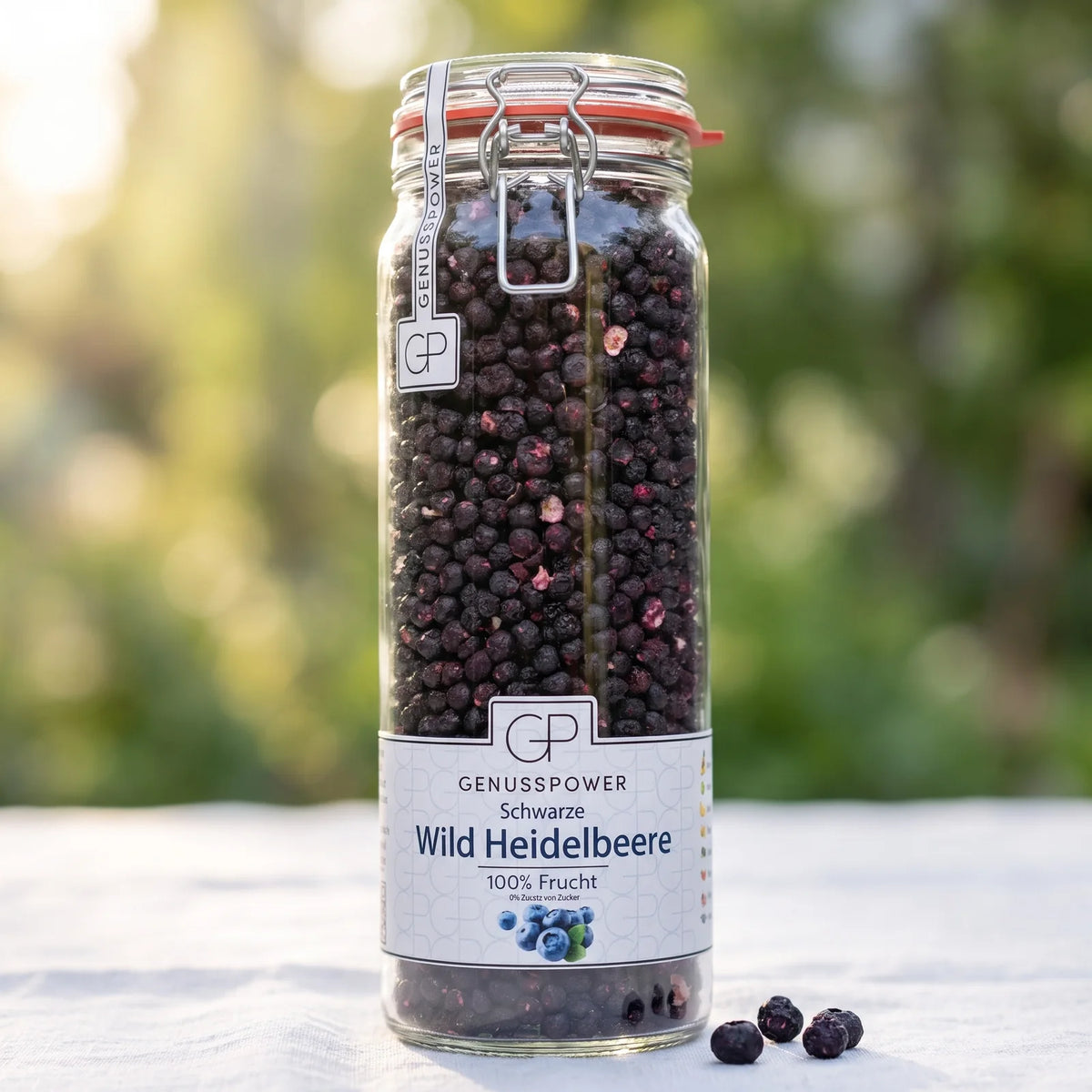 Großes Bügelglas gefriergetrocknete Wild-Heidelbeeren von Genusspower auf einem weißen Gartentisch im Morgenlicht