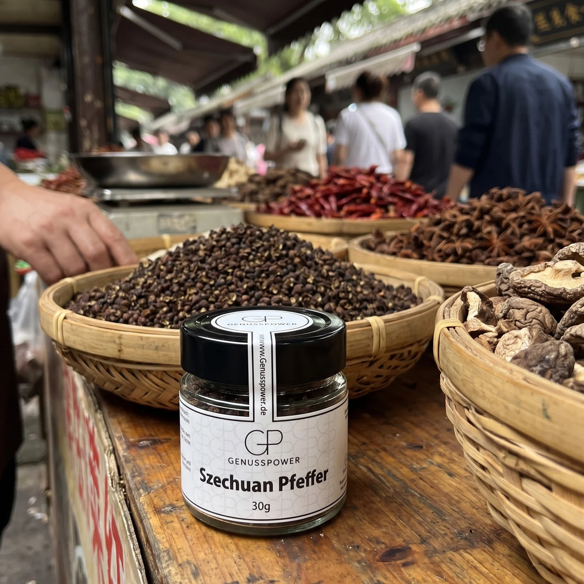 Glas Szechuan Pfeffer von Genusspower am Gewürzstand eines Markts in Chengdu, dahinter Körbe mit dunklem Szechuan Pfeffer