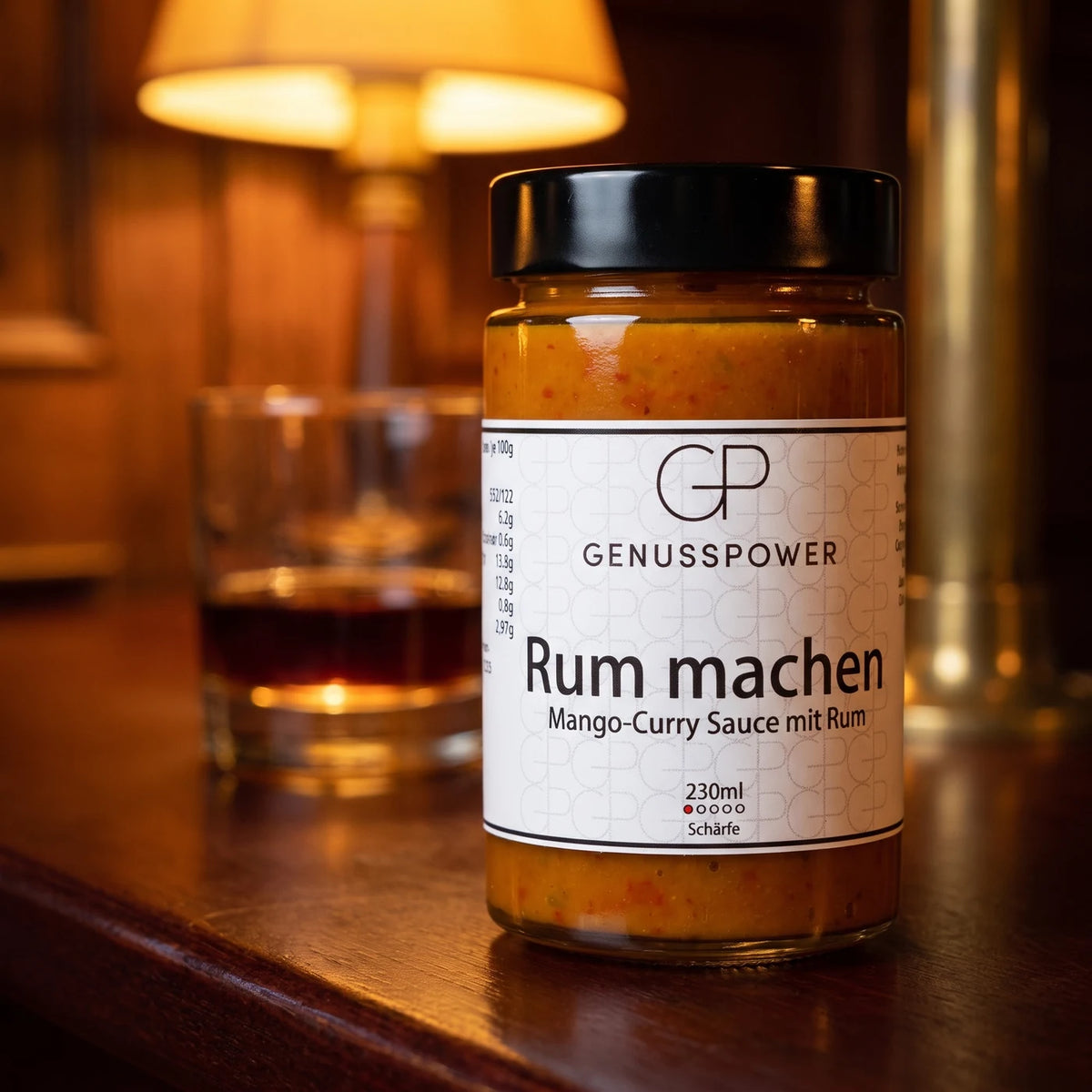 Glas Rum machen auf einem Mahagonitresen im Lampenlicht, dahinter ein Glas dunkler Rum